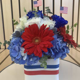 Red, white, and blue flower arrangement in a white box with small American flags