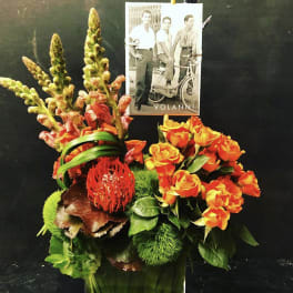 Orange roses and snapdragons arranged in a vase with a photo card