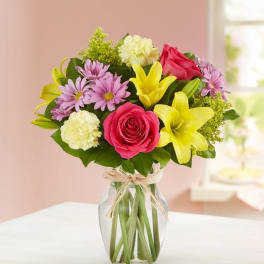 Bouquet of pink roses, yellow lilies, and purple daisies in a glass vase