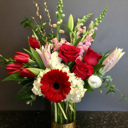 Red roses and lilies arranged in a glass vase with white blooms