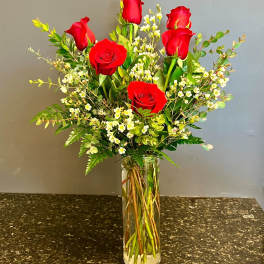 Red roses arranged in a clear glass vase with small white filler flowers