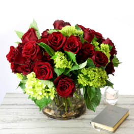 Low arrangement of red roses and green hydrangea in a clear glass vase on a table