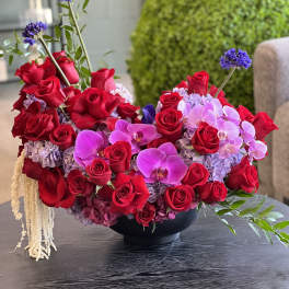 Red roses and pink orchids arranged in a black bowl vase