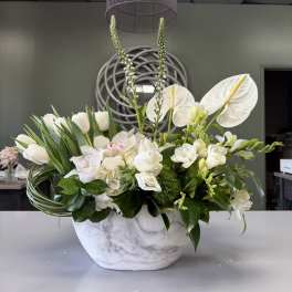 White floral arrangement in a marble-look bowl with tall stems and orchids