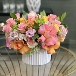 Mixed pink, peach, and yellow roses arranged in a white vase