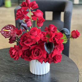 Red rose arrangement with dark calla lilies in a white vase