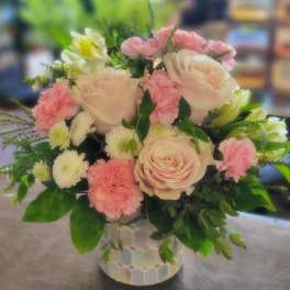Round arrangement of pale pink roses, pink carnations, and white mums in a patterned ceramic vase