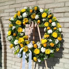 Yellow and white floral wreath on a wooden easel with a white ribbon