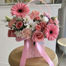 Pink and white flower arrangement in a pink gift bag with ribbon handles
