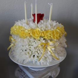 White and yellow floral arrangement with red roses and tall white candles