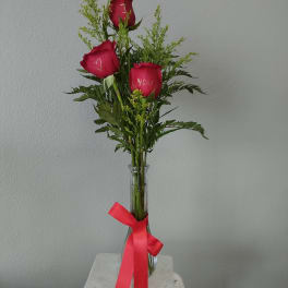 Three red roses in a clear glass vase with a pink ribbon