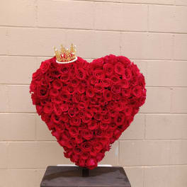 Heart-shaped arrangement of red roses with a small crown topper