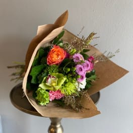 Mixed bouquet with orange, pink, and green flowers wrapped in brown paper