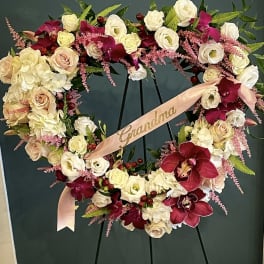 Heart-shaped floral wreath with roses, orchids, and a pink ribbon