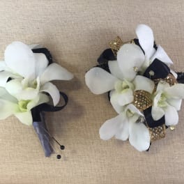 Two white orchid boutonnieres with black and gold accents on burlap