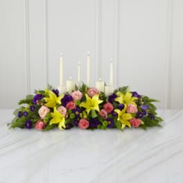 Low floral centerpiece with candles and pink, yellow, and purple flowers