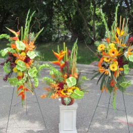 Three tropical floral arrangements with orange and yellow blooms on stands