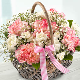 Pink and white carnations in a wicker basket with a gingham ribbon