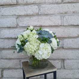 White floral arrangement in a glass vase with green accents