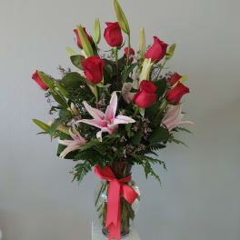 Bouquet of red roses and pink lilies in a glass vase with a ribbon