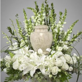 White floral arrangement with lilies and roses around a stone urn