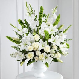 Tall white arrangement of lilies, roses, and other blooms in a white pedestal vase