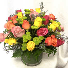 Colorful bouquet of mixed roses and green button mums arranged in a clear glass cylinder vase.