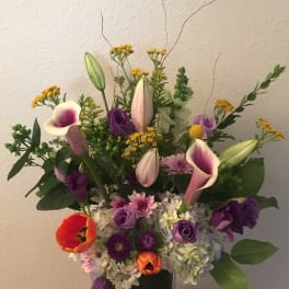 Mixed bouquet with purple flowers, calla lilies, and orange tulips in a vase