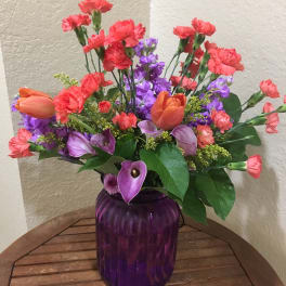 Colorful bouquet with orange tulips, purple flowers, and pink carnations in a purple vase