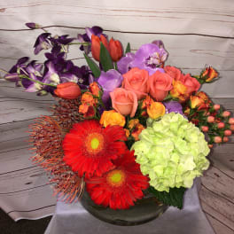 Colorful mixed bouquet with roses, orchids, gerbera daisies, and hydrangea in a glass vase