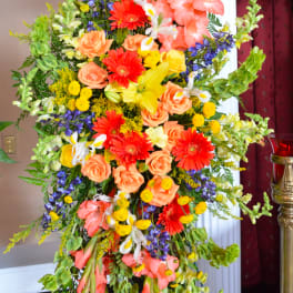 Tall floral standing spray with orange, yellow, purple, and white blooms