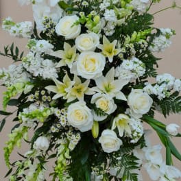 White floral standing spray with roses and lilies on a black easel