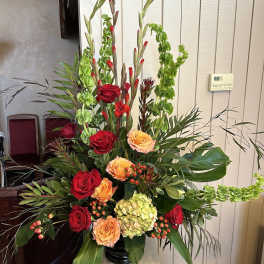 Tall arrangement of red and peach roses with green hydrangea and Bells of Ireland in a black vase