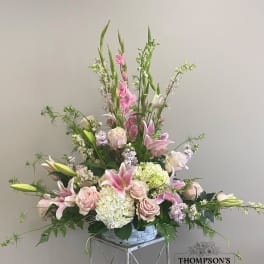 Tall pastel arrangement of pink lilies, roses, and white hydrangeas in a white basket.