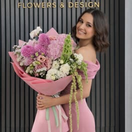 Woman holding a large pink bouquet in front of a flower shop sign