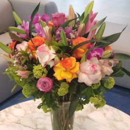 Mixed bouquet of roses, lilies, and orchids in a clear glass vase