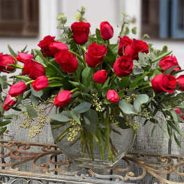 Red roses arranged in a clear glass vase with eucalyptus
