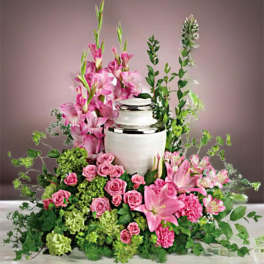 Pink floral arrangement around a white urn with lilies and roses