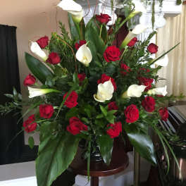 Large arrangement of red roses and white calla lilies in a dark pedestal vase