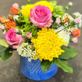 Bright mixed bouquet of pink roses, yellow mums, and small white blooms in a blue ceramic vase