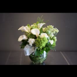 White calla lilies and green-white flowers in a glass vase