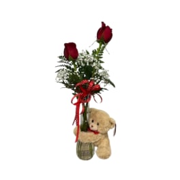 Two red roses in a glass vase with baby's breath and a teddy bear