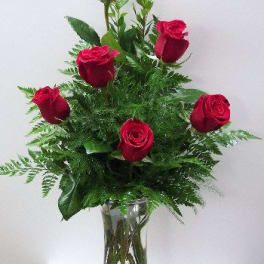 Red roses arranged in a clear glass vase with greenery