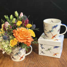 Orange and yellow flower arrangement in a dragonfly mug beside a matching mug and box
