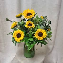 Arrangement of bright yellow sunflowers with abundant foliage in a clear glass vase