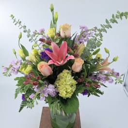 Mixed arrangement of pink lilies, roses, and pastel flowers in a clear glass vase
