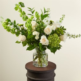 Tall arrangement of white roses and green hydrangea in a clear glass vase