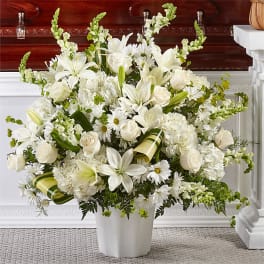 Large white funeral arrangement of lilies, roses, and daisies in a white container