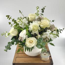 Cream rose and white flower arrangement in a white vase with a candle