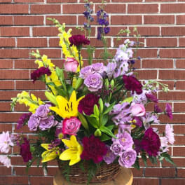 Mixed bouquet of yellow lilies, purple roses, and pink flowers in a basket